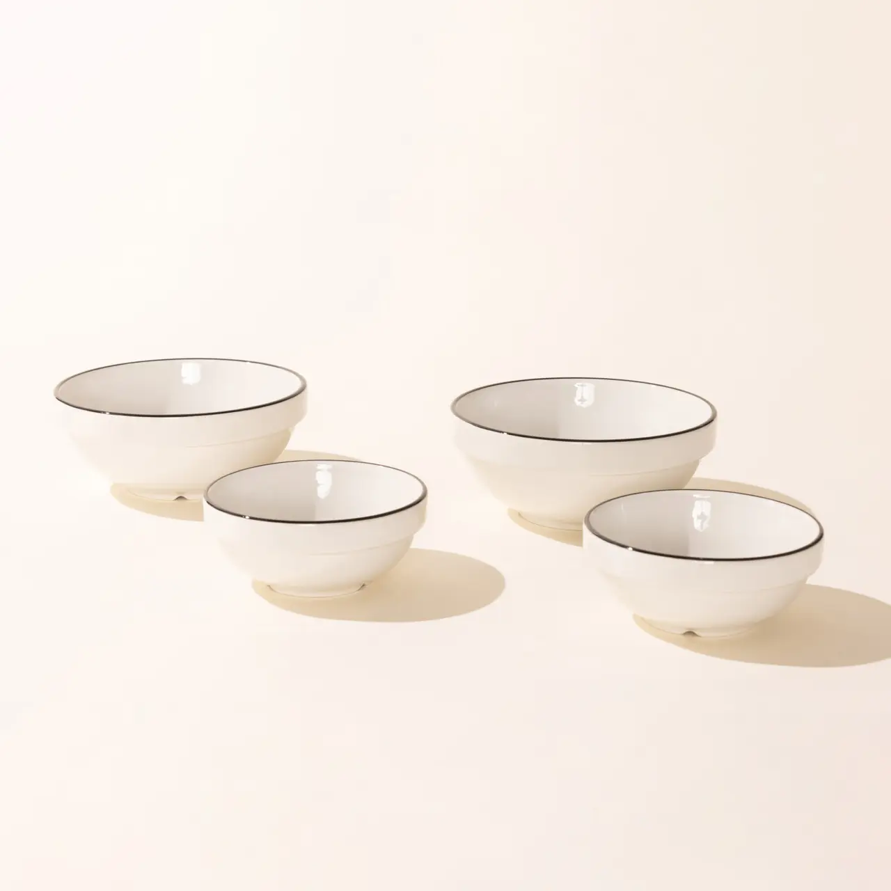 Four white ceramic bowls are arranged in a staggered line against a light beige background.