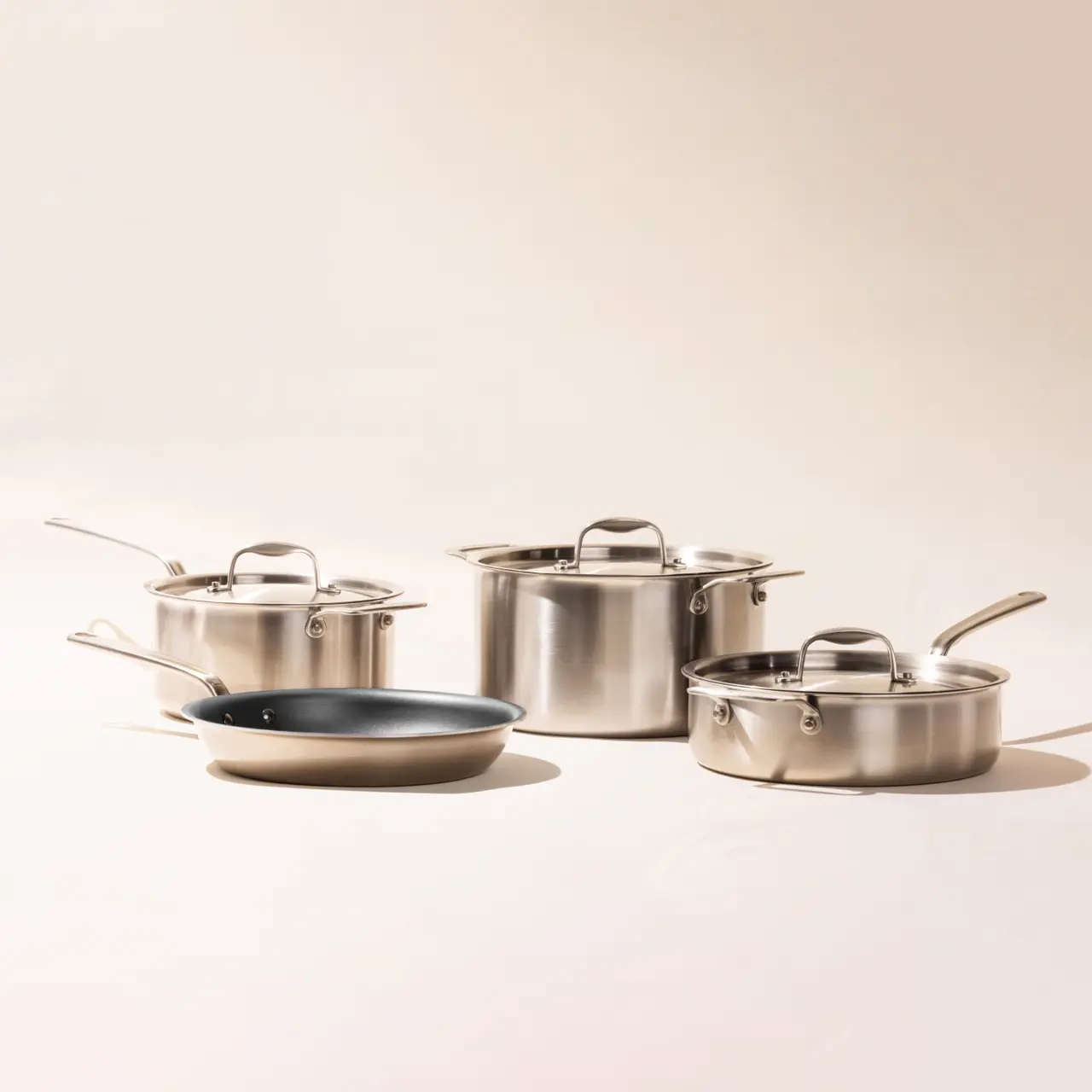 A set of stainless steel cookware, including pots and a pan, is neatly arranged on a light background.
