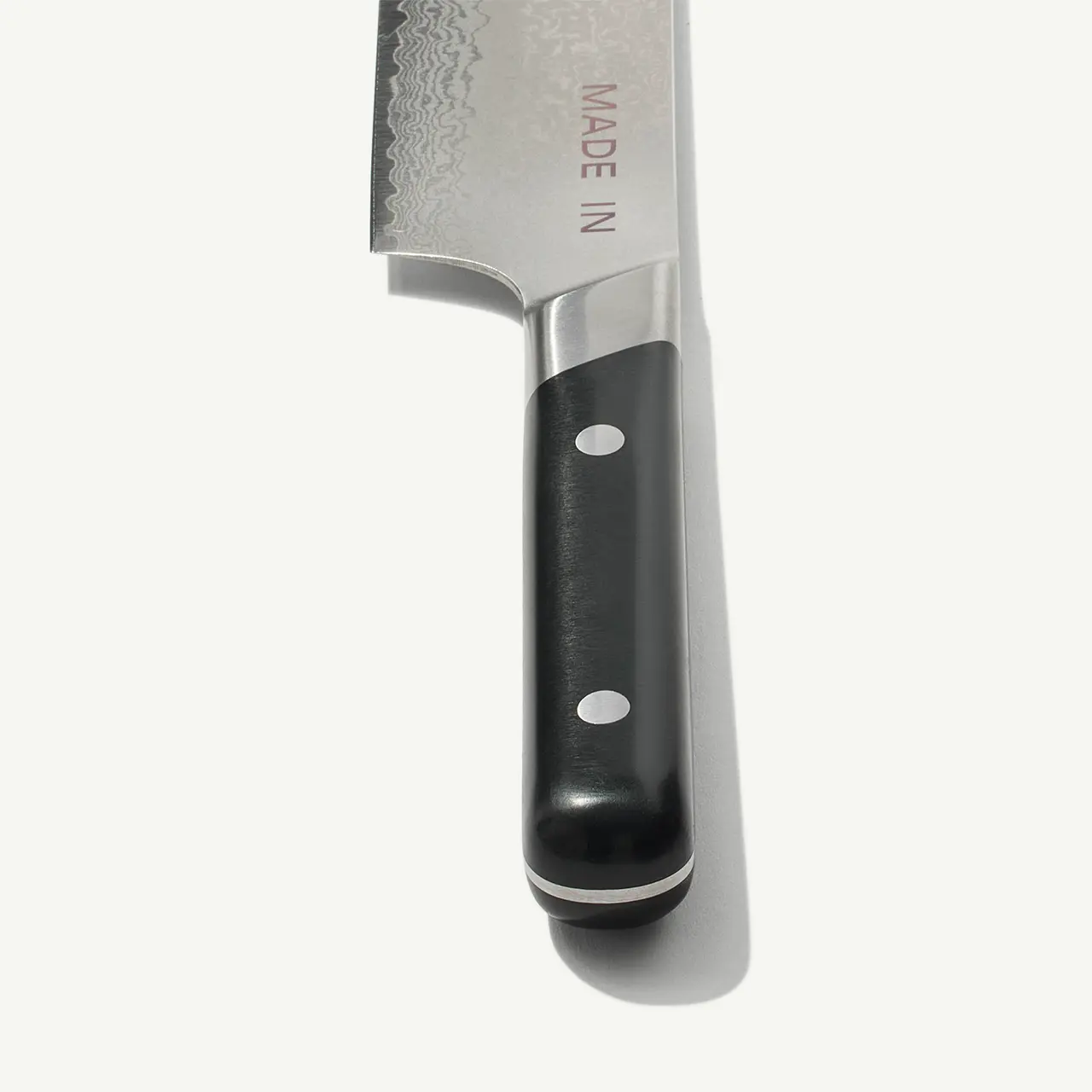 A chef's knife with a black handle and visible text on the blade reading "MADE IN" is photographed against a white background.