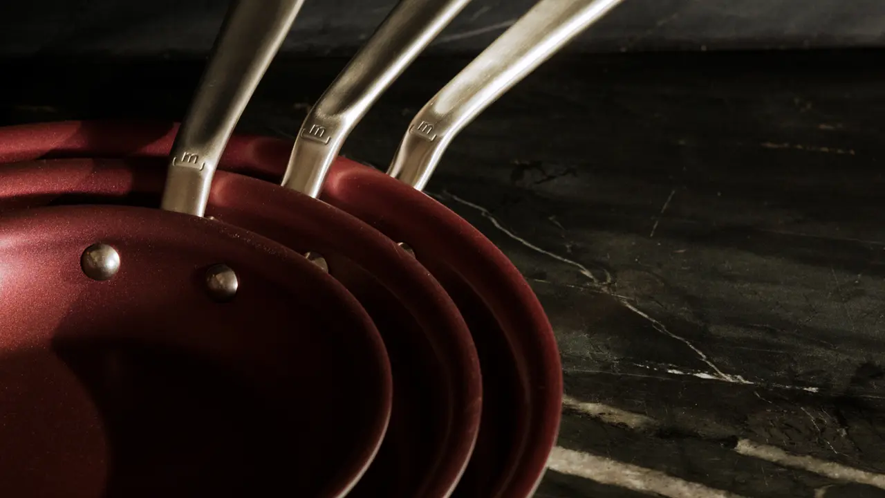 A set of red pans with silver handles neatly stacked on a dark surface.