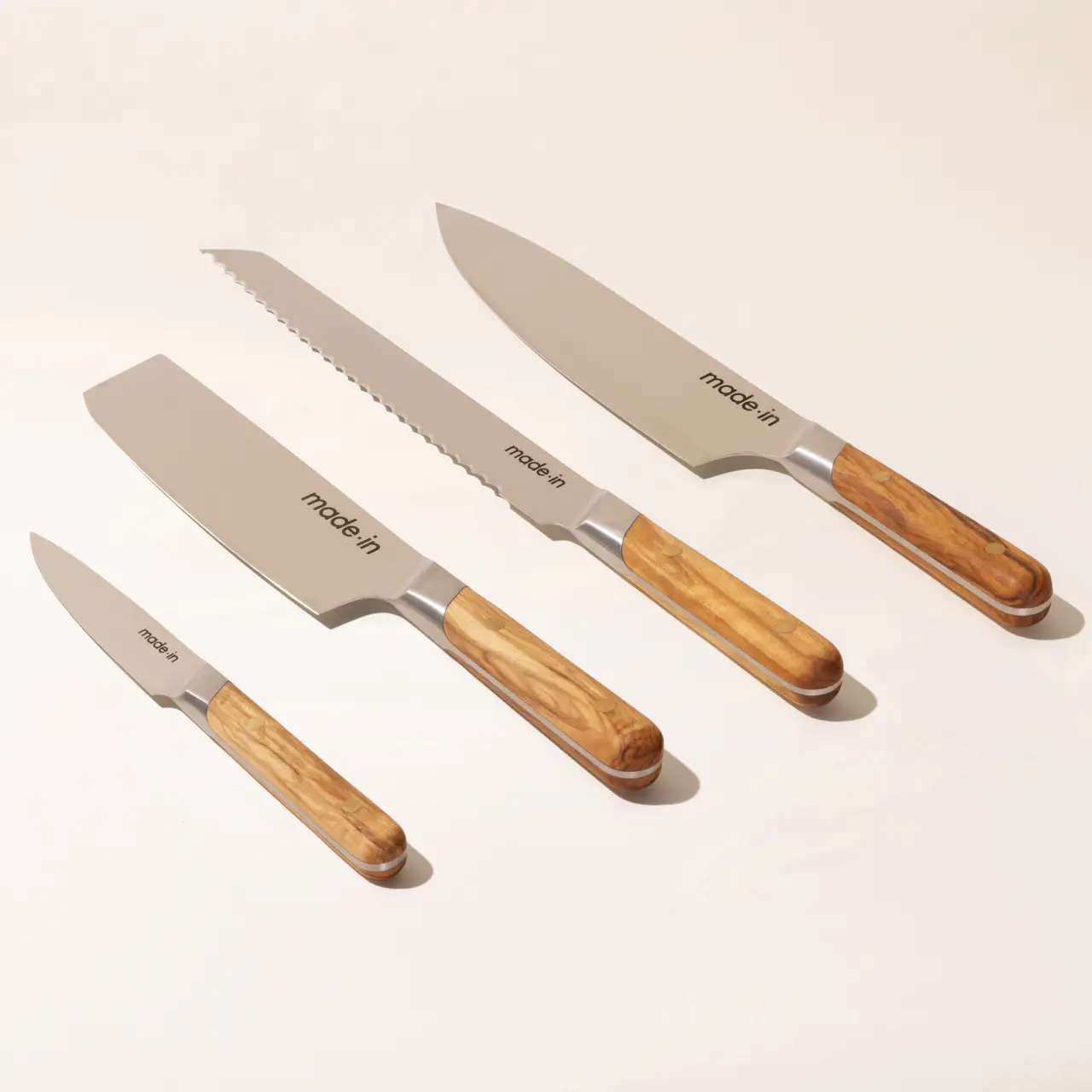 A set of four kitchen knives with wooden handles arranged by size on a light background.