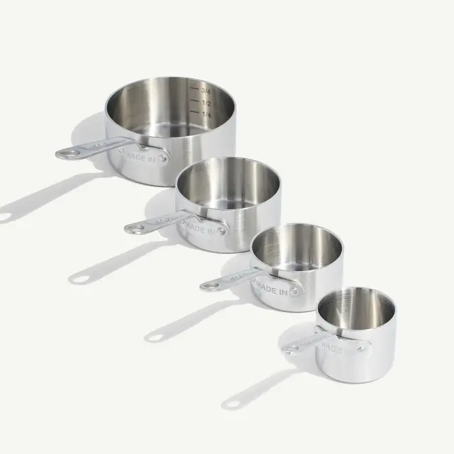 Four stainless steel measuring cups of different sizes are arranged in descending order.