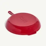 A red frying pan is placed upside down on a white surface.