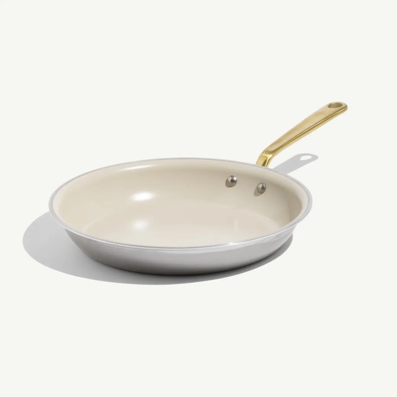 A white, non-stick frying pan with a gold handle rests on a light background.