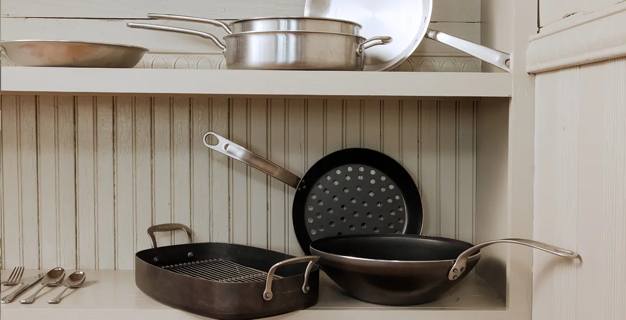 An open kitchen cabinet displaying a neat arrangement of various pots, pans, and cooking utensils.