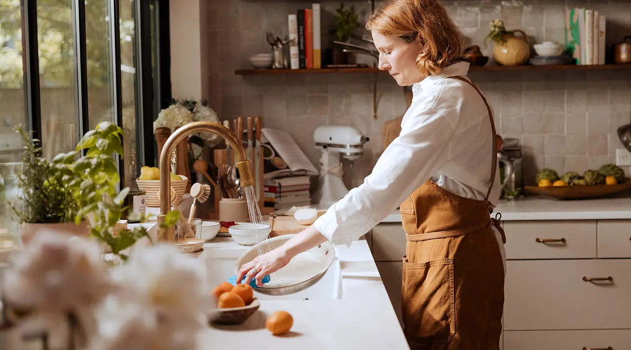 A person wearing an apron is cracking eggs into a bowl on a kitchen counter, surrounded by various cooking utensils and ingredients.