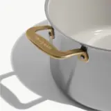 A sleek stainless steel pot with a gold handle and a smooth inner surface, casting a soft shadow on the surface below.