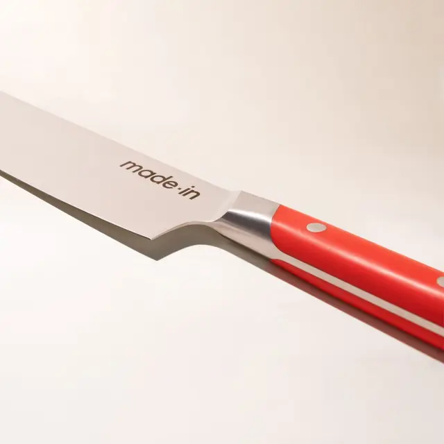 A close-up of a chef's knife with a red handle and the text "made in" on the blade, implying the brand name, isolated against a white background.