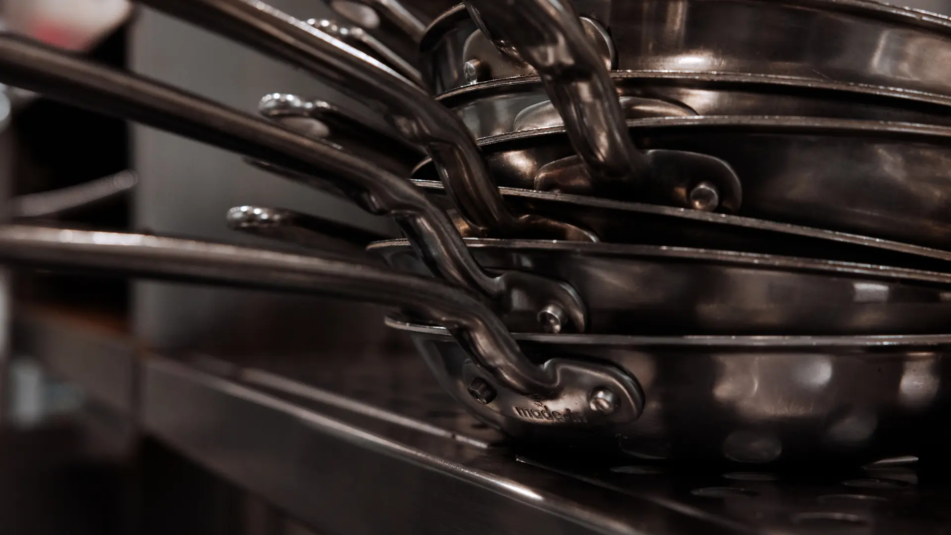 A stack of stainless steel frying pans with long handles rests on a countertop.