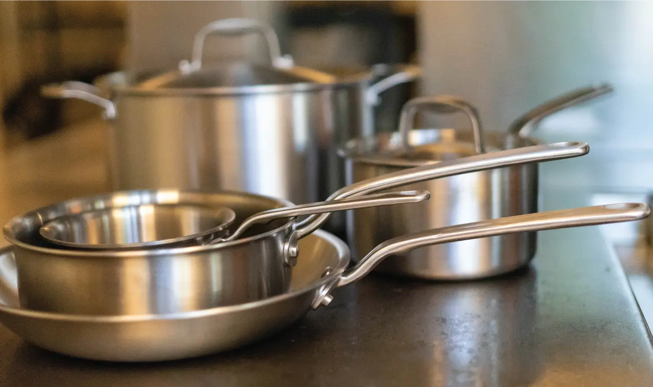 A collection of stainless steel pots and pans with metallic lids on a kitchen counter.