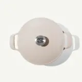 A round, cream-colored cast iron Dutch oven with a stainless steel knob on the lid is displayed against a light background.