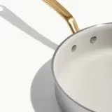 A sleek gray saucepan with a gold handle is positioned against a light background, showcasing its smooth, empty interior.