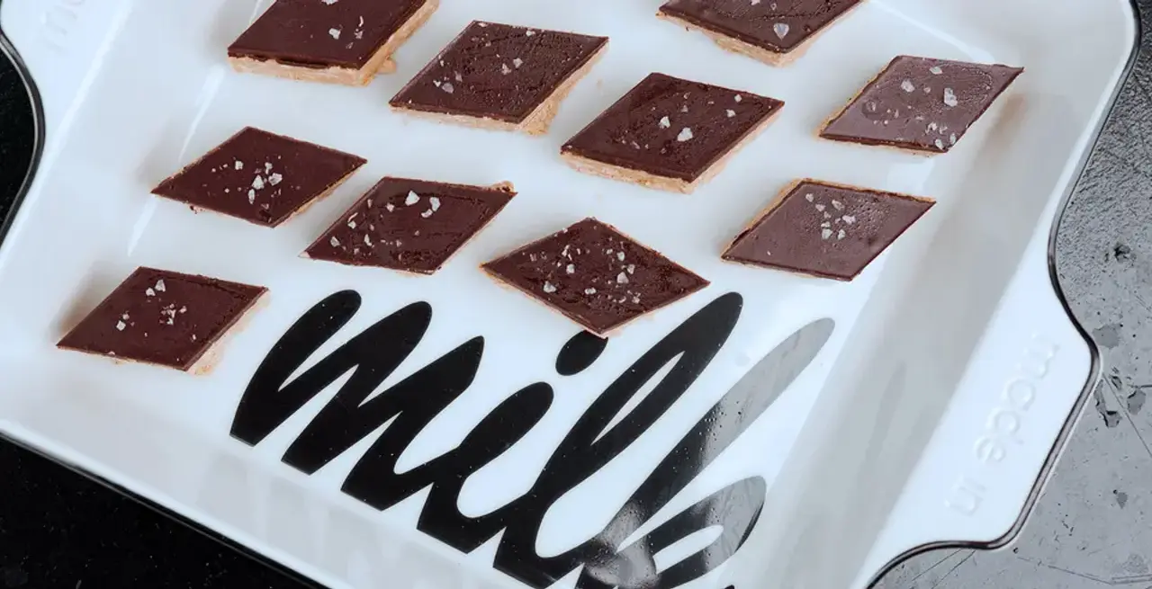 A white serving platter with the word "milk" written on it, partially covered by evenly spaced chocolate-topped biscuits with visible salt sprinkles.