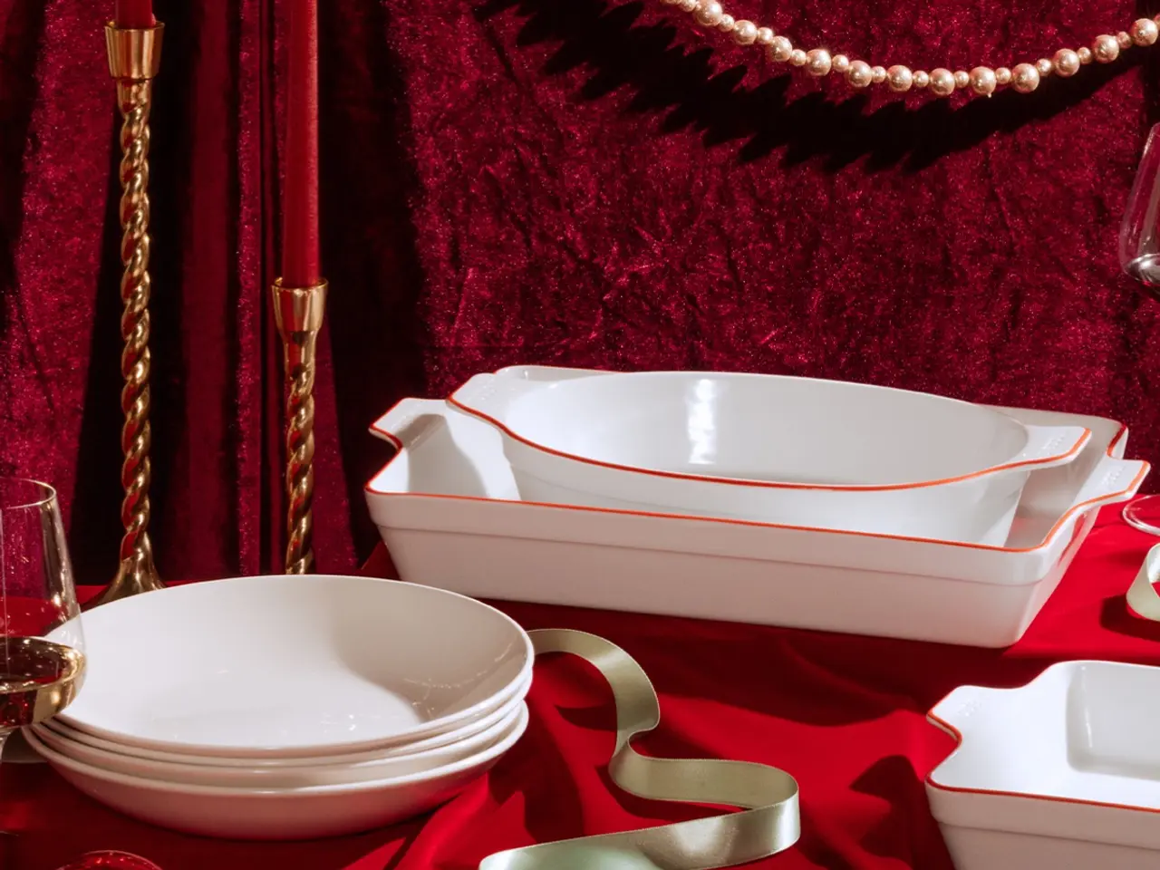 A luxurious table setting featuring white dishes with gold trim, elegant glassware, and golden accents on a red velvet cloth.