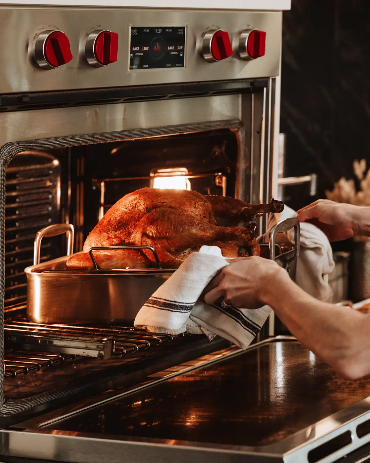 A person is pulling a roasting pan with a golden-brown turkey out of an oven.