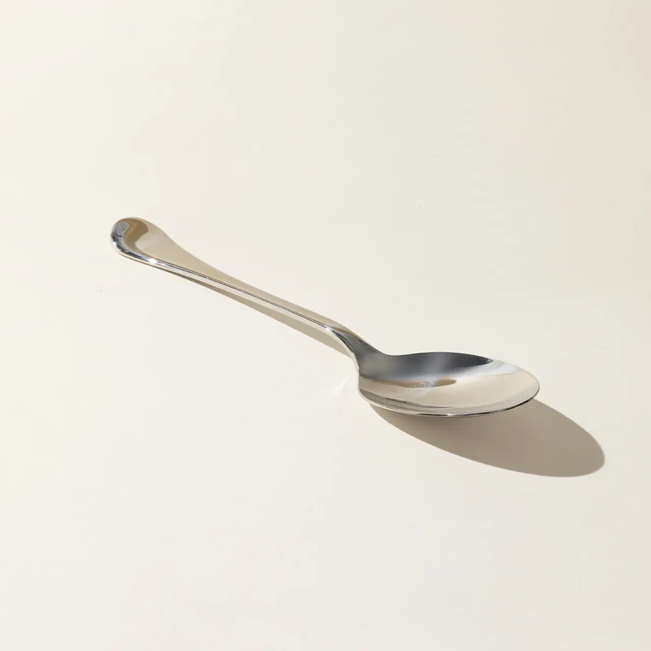 A silver spoon casting a shadow on a light surface.