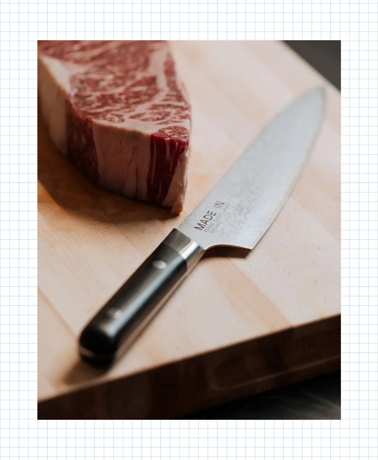 A sharp kitchen knife lies next to a raw marbled steak on a wooden cutting board.