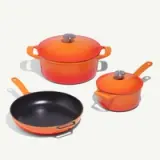 A set of three vibrant orange cooking pots and pans, including a large dutch oven, a smaller saucepan, and a frying pan.
