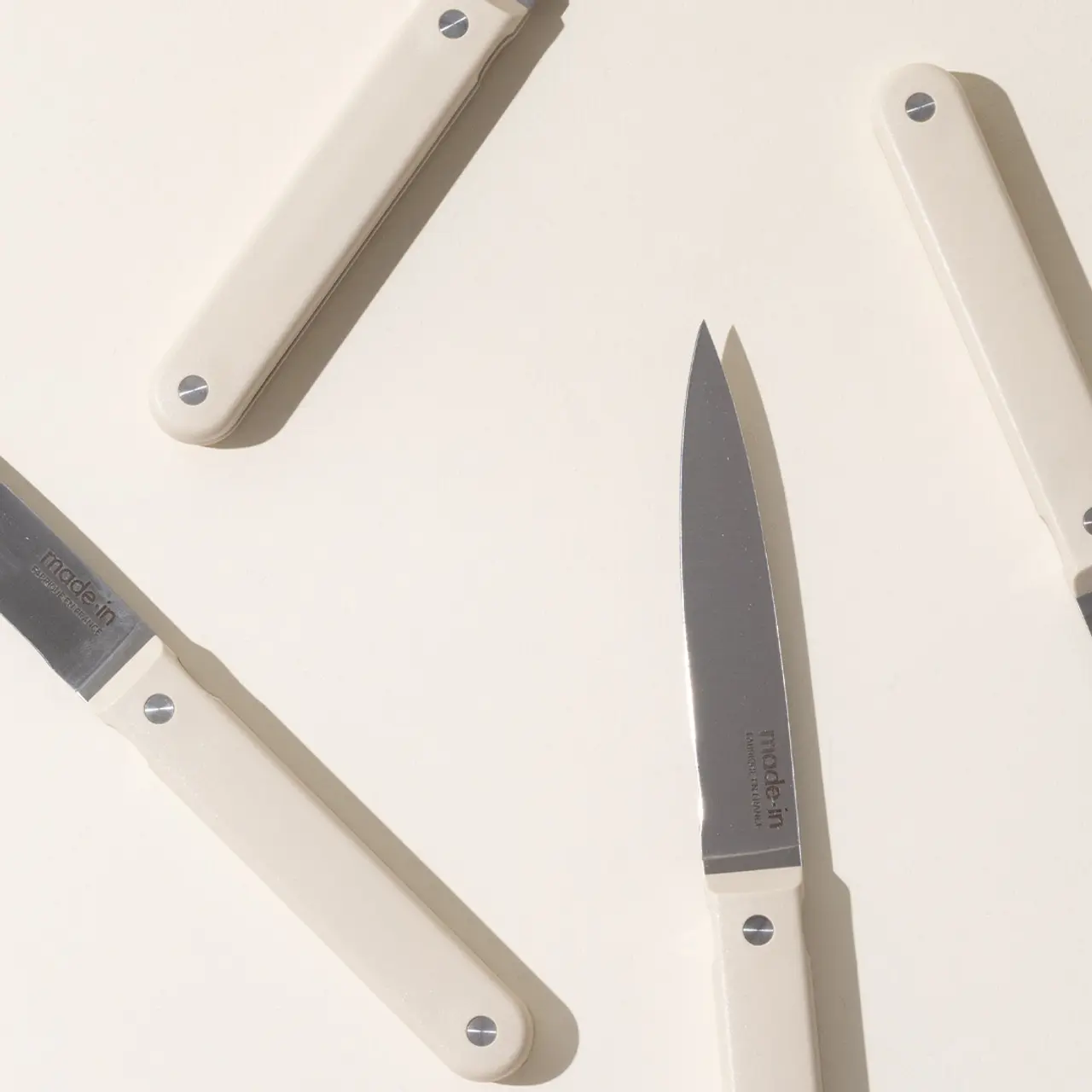 Four folding knives with ivory-colored handles are placed at different angles on a plain surface.