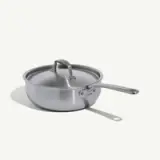 A stainless steel saucepan with a lid and a long handle is placed against a plain background.