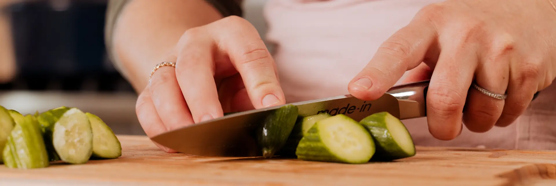 A person is slicing cucumber on a wooden cutting board.