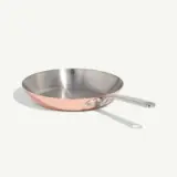 A copper-bottomed stainless steel skillet with a long handle is shown against a plain background.