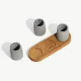 Three stone-like cylindrical objects sit beside a rounded wooden tray with fitted depressions.