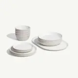 A minimalist set of white ceramic bowls, plates, and saucers are neatly stacked against a plain background.