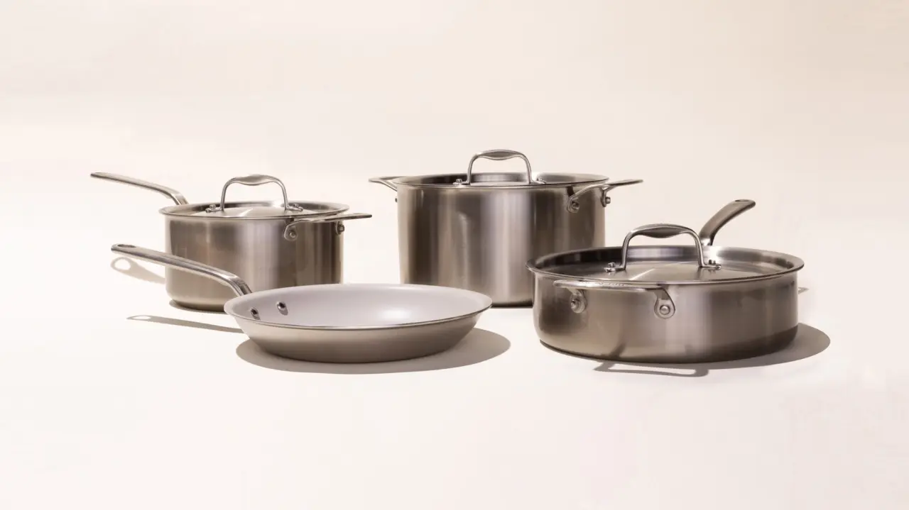 A set of four stainless steel cooking pots and a frying pan on a light background.