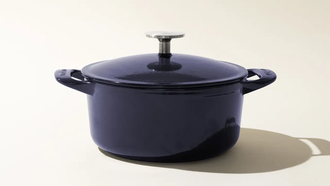 A navy blue enameled cast iron Dutch oven with the lid on, set against a light background with a soft shadow to the right.