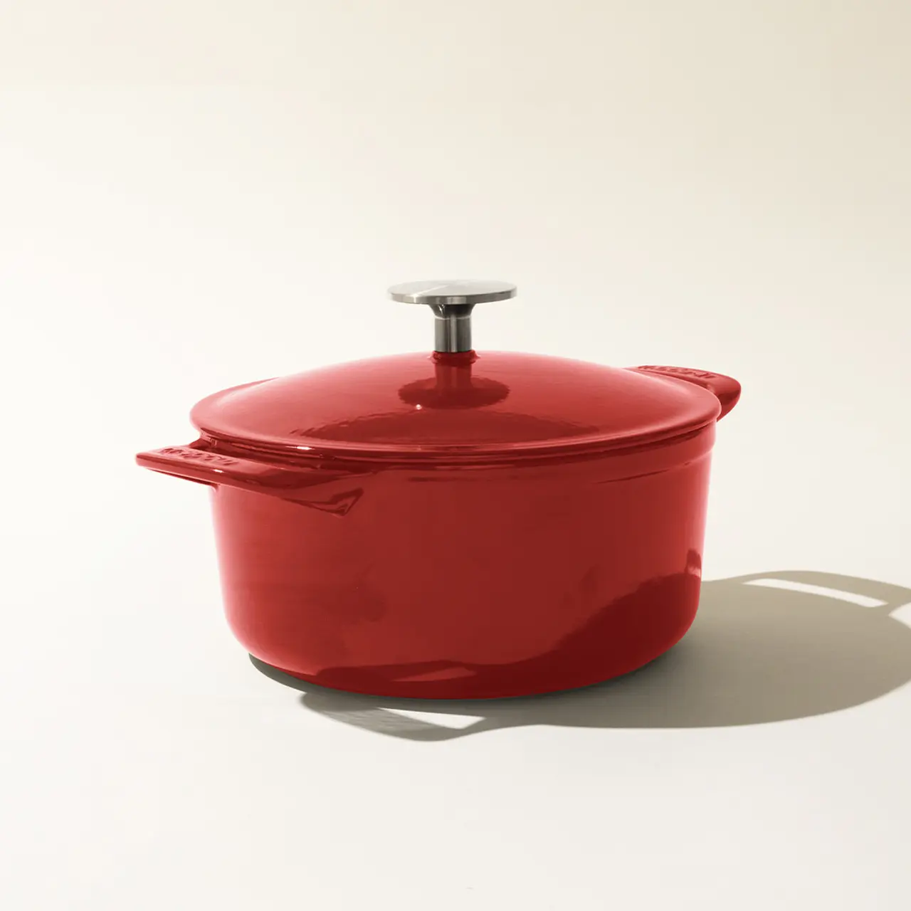 A red enameled cast-iron Dutch oven with a lid, on a light background casting a soft shadow.