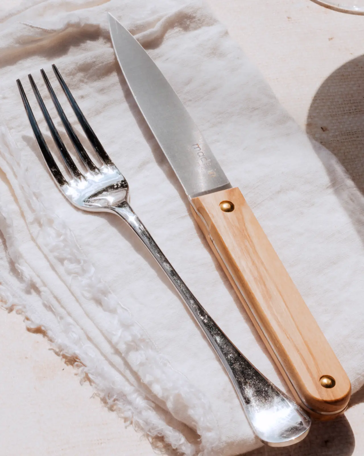 A fork and a knife with a wooden handle rest on a white cloth napkin.