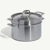 A stainless steel pot with a lid and a built-in steamer insert is shown on a white background.