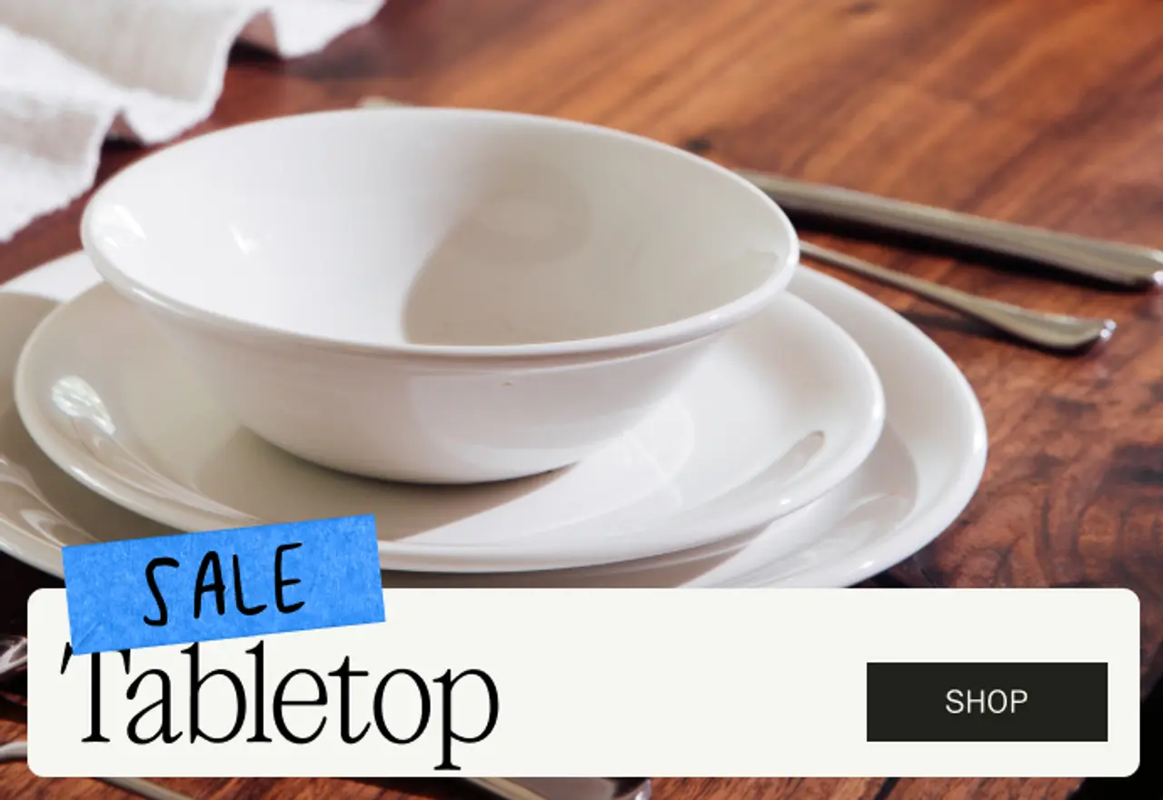 A stacked arrangement of white dishes is displayed on a wooden table, accompanied by a promotional banner for a tabletop sale.