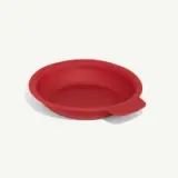 A red, round silicone baking dish with a handle on one side is displayed against a white background.