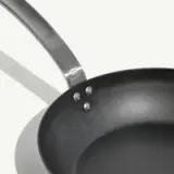 A black frying pan with a metal handle is shown against a light background.