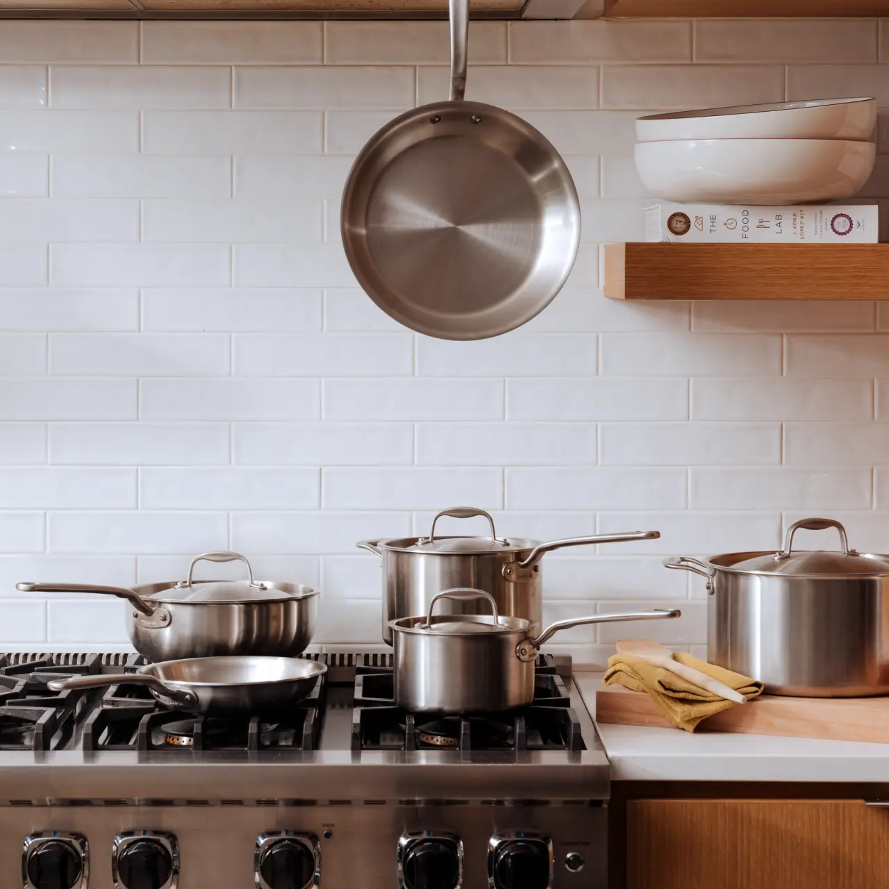 A tidy kitchen with a variety of pots on a stove and one hanging above, showcasing a clean cooking environment.