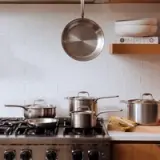 A tidy kitchen with a variety of pots on a stove and one hanging above, showcasing a clean cooking environment.