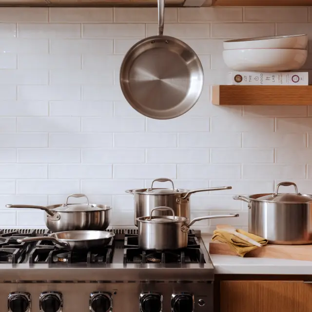 A tidy kitchen with a variety of pots on a stove and one hanging above, showcasing a clean cooking environment.