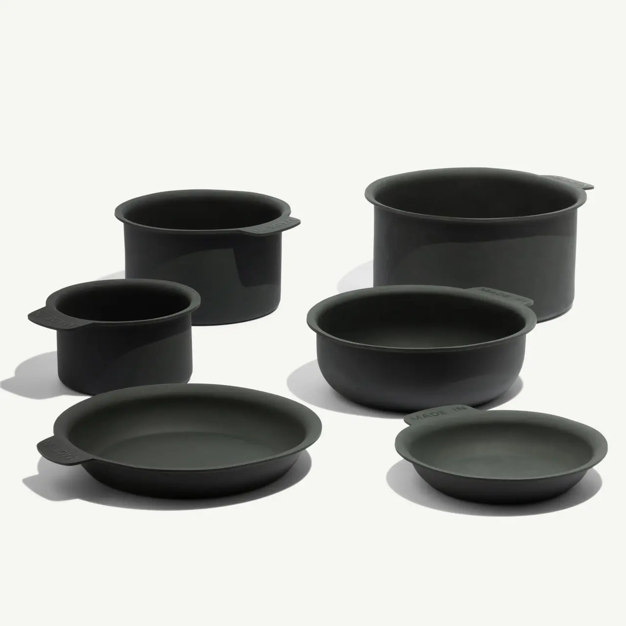 A collection of six green kitchen pots and pans in various sizes and shapes, featuring ergonomic handles.