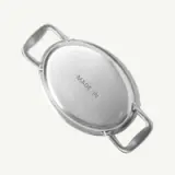 A shiny, oval metal serving dish with two handles and the text "MADE IN" engraved on the bottom.