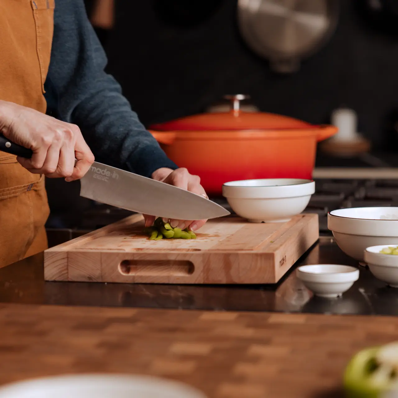 A person is chopping vegetables on a wooden cutting board in a kitchen setting.