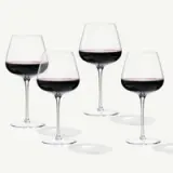 Four elegant wine glasses filled with red wine are arranged against a light background.