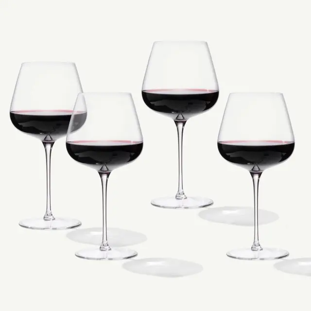 Four elegant wine glasses filled with red wine are arranged against a light background.