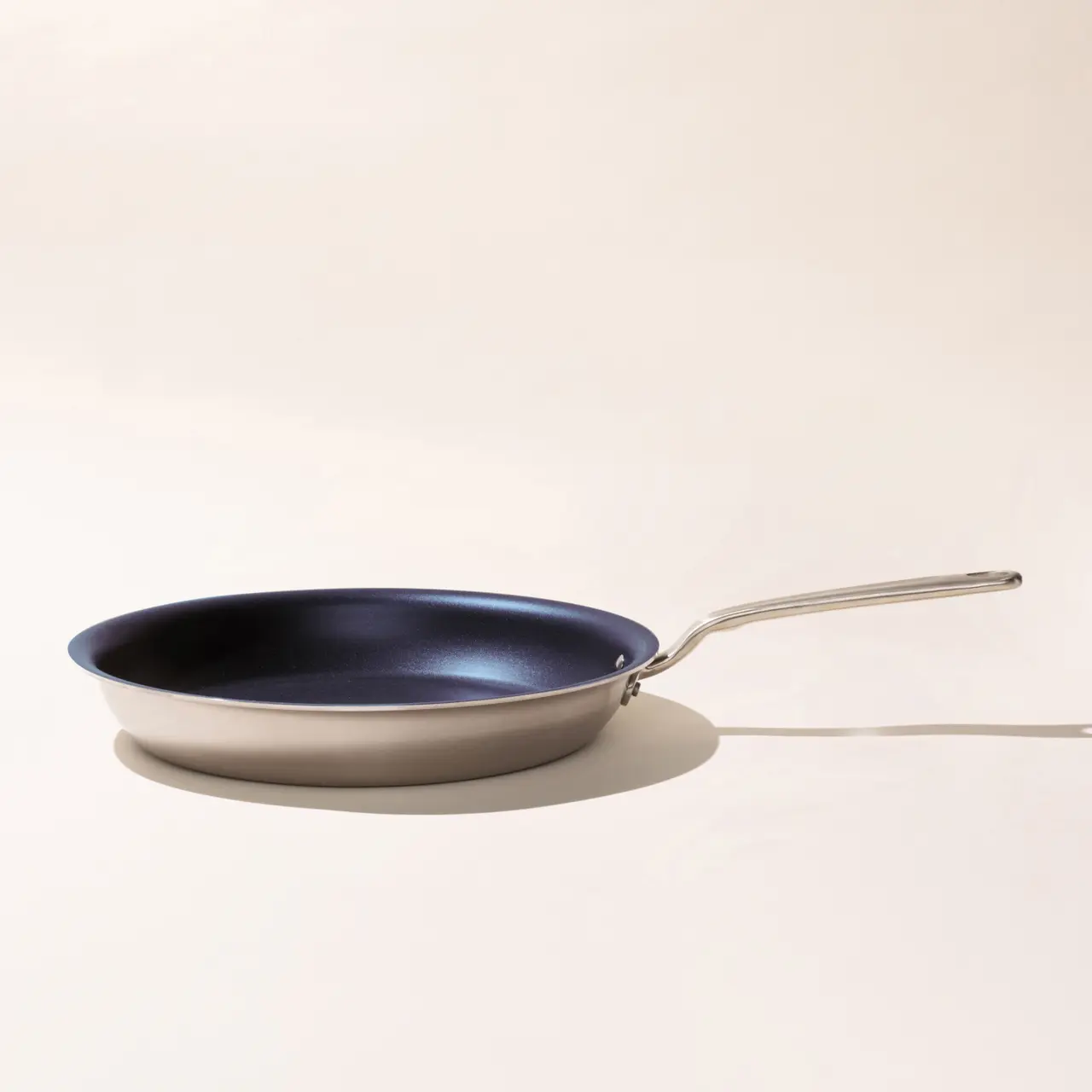A modern frying pan with a silver handle on a light background, casting a soft shadow.