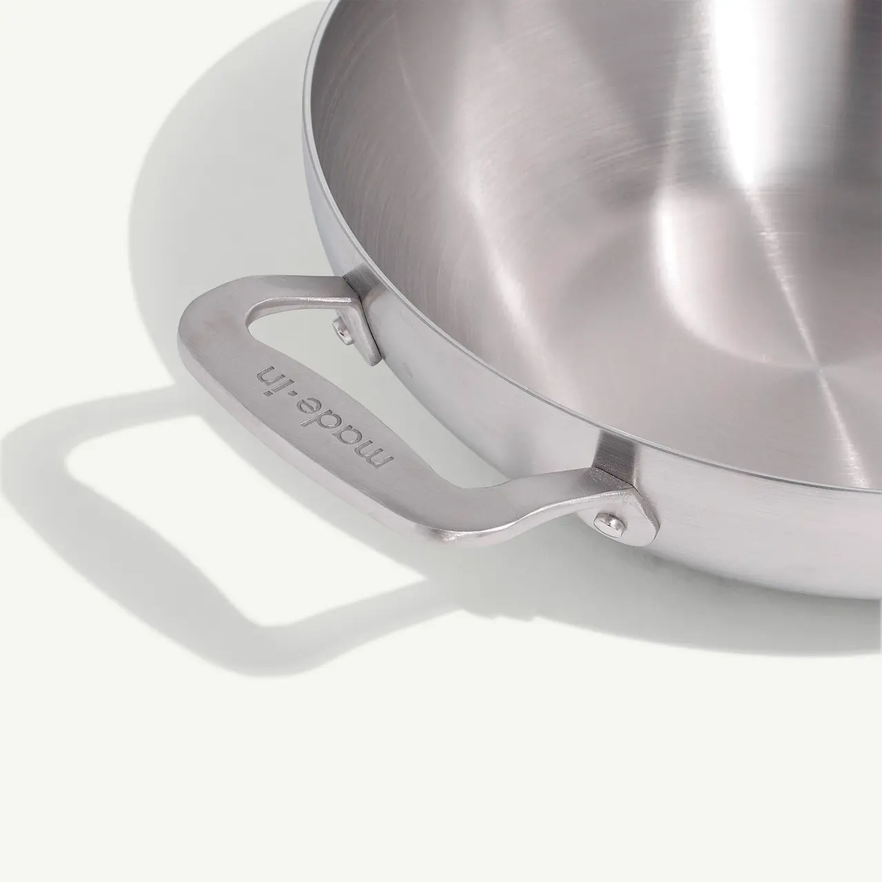 A stainless steel pot casts a sharp shadow on a light surface, emphasizing the detail on its handle.