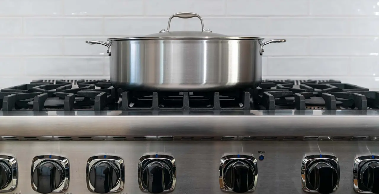 A stainless steel pot sits on a gas stove top with multiple control knobs in a kitchen setting.
