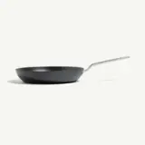 A black frying pan with a silver handle is positioned on a light background.