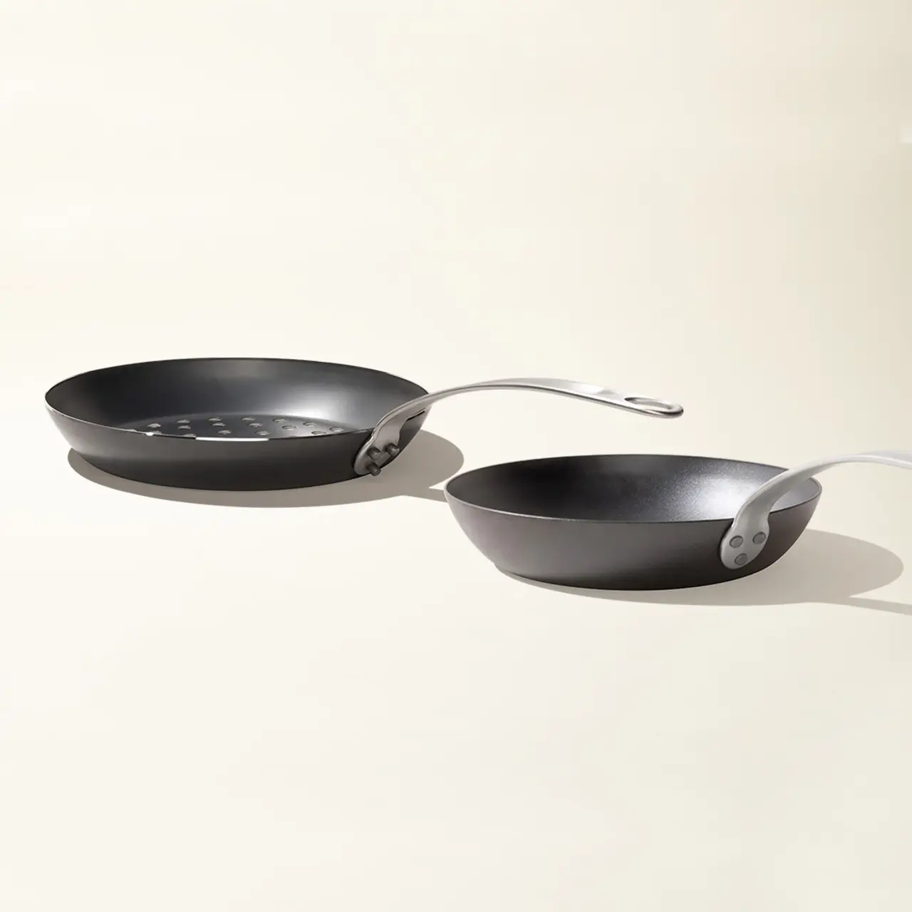 Two black non-stick frying pans with silver handles are positioned side by side on a light background.