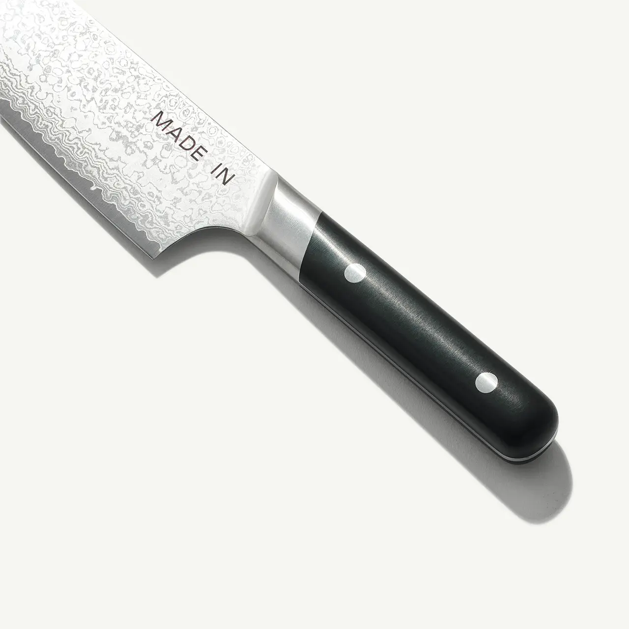 A chef's knife with a patterned blade and a black handle lies against a light background.